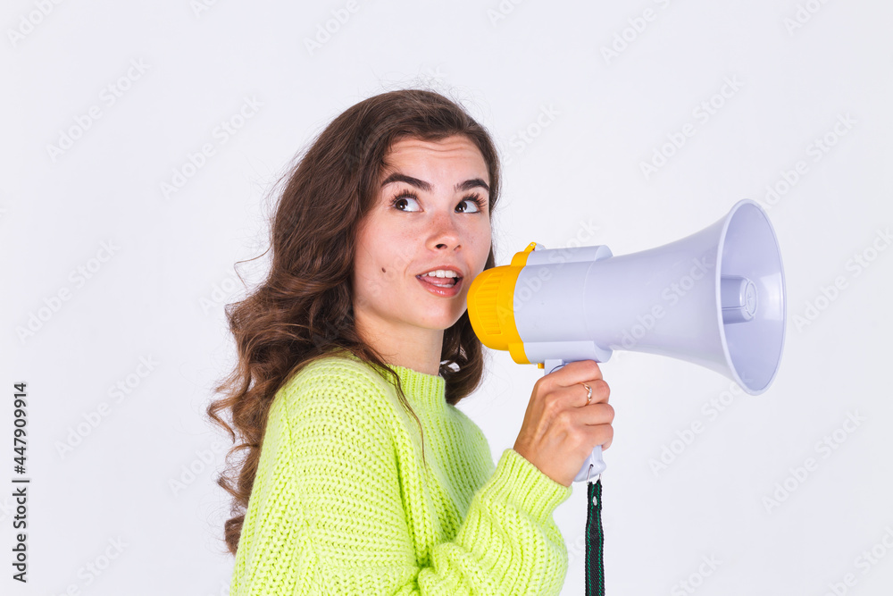 Young beautiful woman with freckles light makeup in sweater on white background with megaphone shouting screaming Young beautiful woman with freckles light makeup in sweater on white background with megaphone shouting screaming