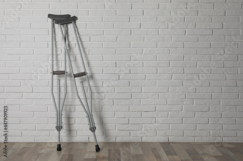 Pair of axillary crutches near white brick wall. Space for text photo