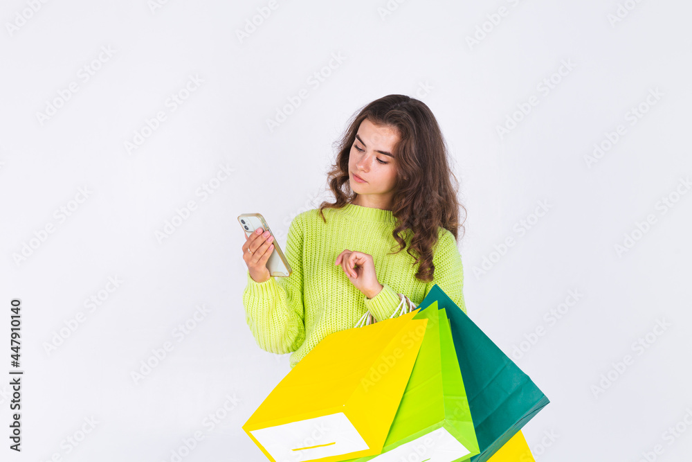 Young beautiful woman with freckles light makeup in sweater on white background with shopping bags and mobile phone Young beautiful woman with freckles light makeup in sweater on white background with shopping bags and mobile phone