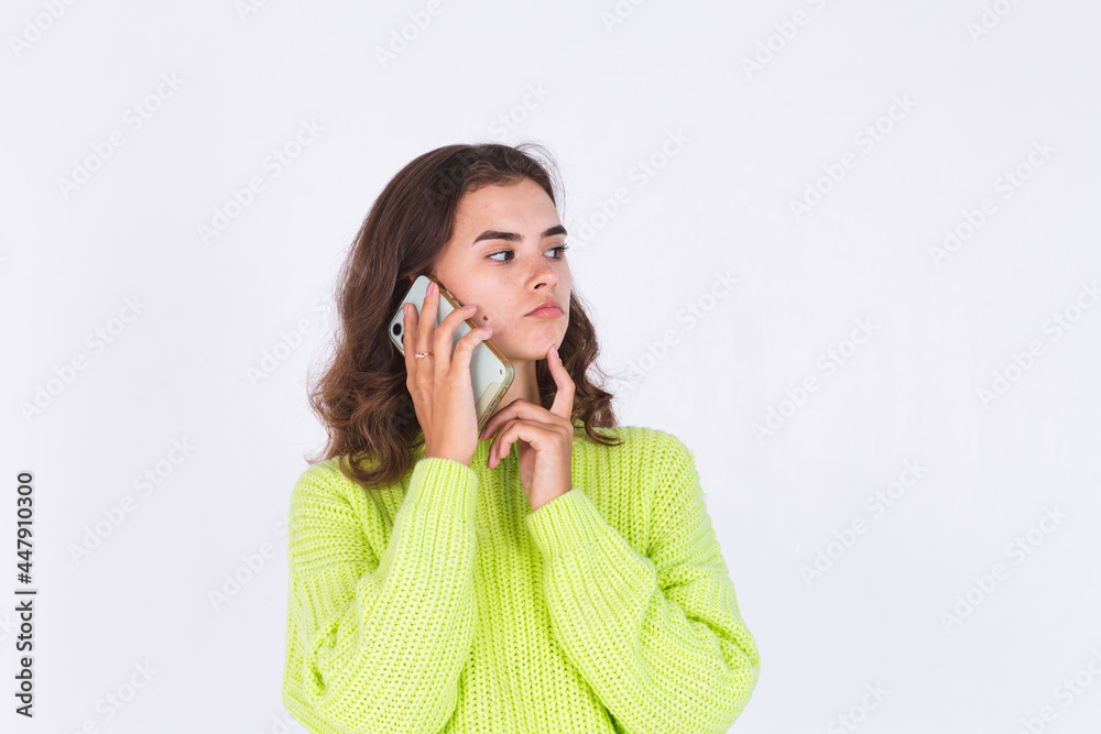 Young beautiful woman with freckles light makeup in sweater on white background with mobile phone thoughtful finger on chin Young beautiful woman with freckles light makeup in sweater on white background with mobile phone thoughtful finger on chin