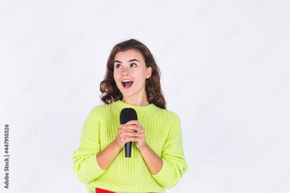 Young beautiful woman with freckles light makeup in sweater on white background with microphone happy singing moving Young beautiful woman with freckles light makeup in sweater on white background with microphone happy singing moving