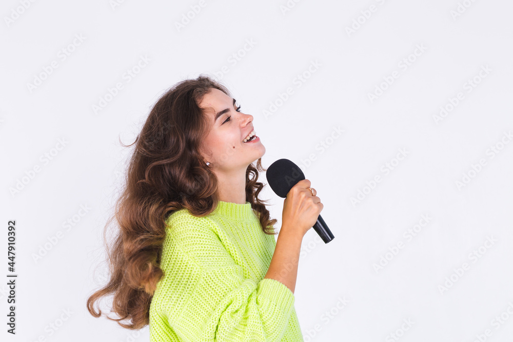 Young beautiful woman with freckles light makeup in sweater on white background with microphone happy singing moving Young beautiful woman with freckles light makeup in sweater on white background with microphone happy singing moving