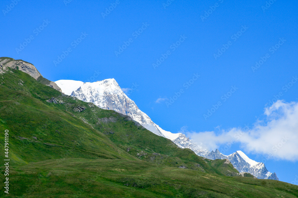 View of the Mont Blanc massif. Snowcapped rocky peak. View of a mountain range in summer or winter with snow at the top. Pastures in the foreground.