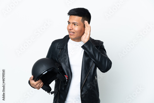 Ecudorian man with a motorcycle helmet isolated on white background listening to something by putting hand on the ear