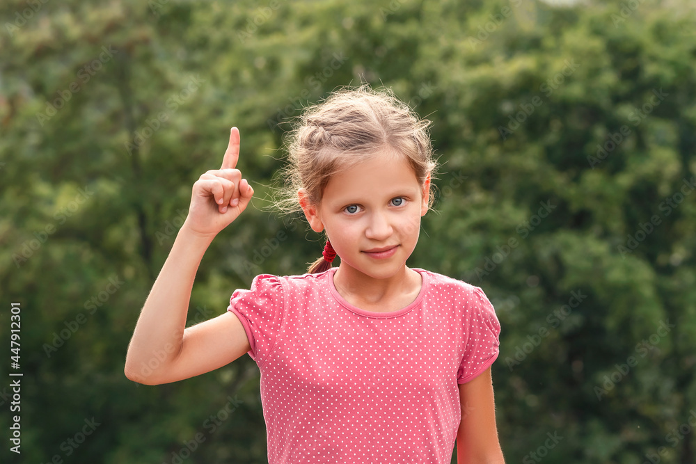 Girl thumb up index finger on greenery background. Kid shows warning sign. Girl thumb up index finger on greenery background. Kid shows warning sign.