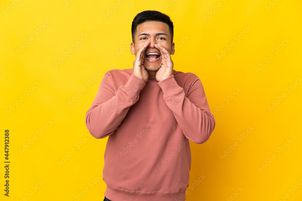 Young Ecuadorian man isolated on yellow background shouting and announcing something Young Ecuadorian man isolated on yellow background shouting and announcing something
