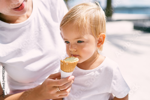 Mom feeds ice cream to little girl. Portrait