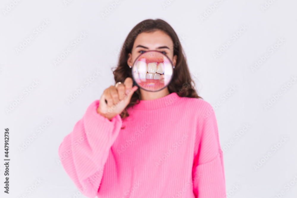 Young beautiful woman with freckles light makeup in sweater on white background with magnifier shows white teeth perfect smile Young beautiful woman with freckles light makeup in sweater on white background with magnifier shows white teeth perfect smile