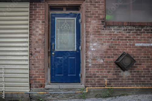 Fotografie Exterior wall of building with weathered red brick, dented blue metal entrance d