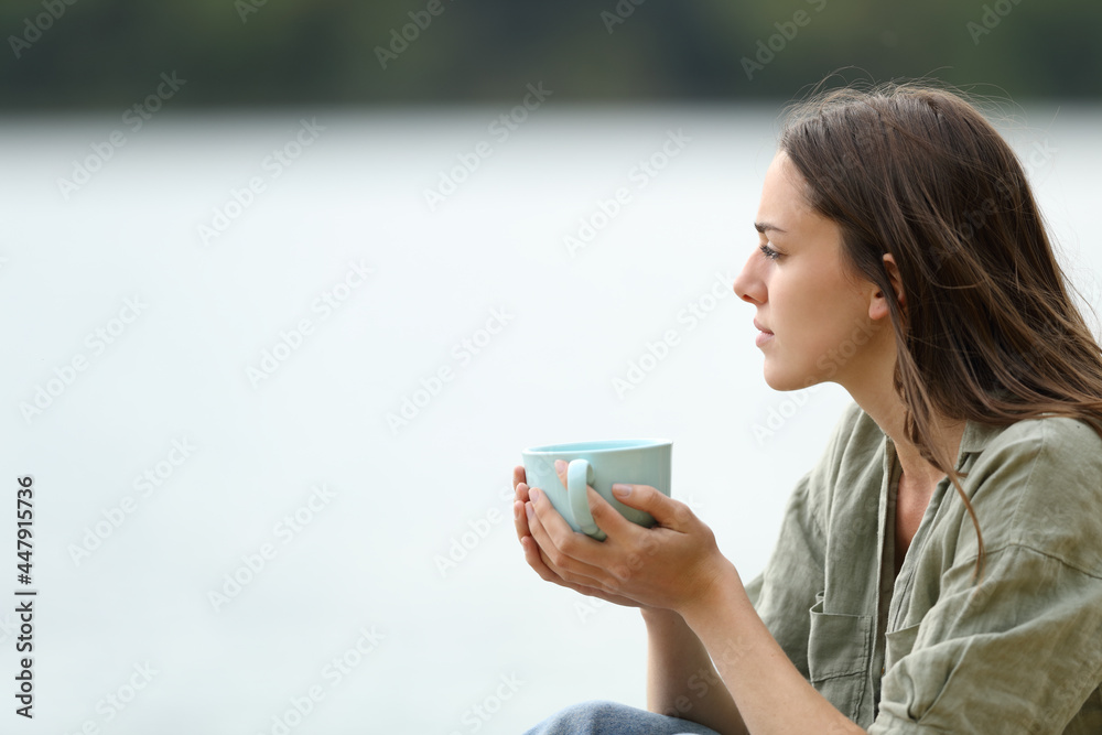 Woman holding coffee cup contemplating a lake Woman holding coffee cup contemplating a lake
