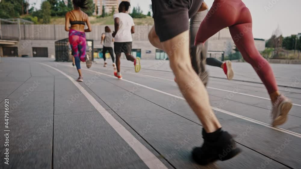 Group of people jogging together at sunrise. Back view of big team of athletes has a group training session on the urban streets of a big city Group of people jogging together at sunrise. Back view of big team of athletes has a group training session on the urban streets of a big city