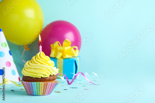Delicious birthday cupcake with candle  near gift box and party hat on light blue background  space for text