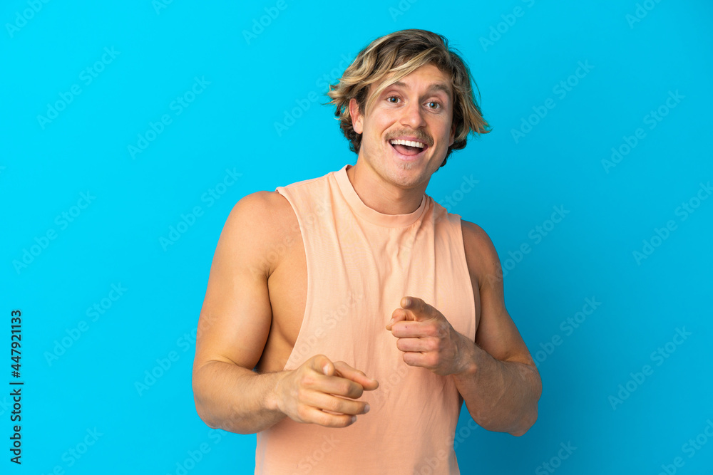 Obraz premium Handsome blonde man isolated on blue background surprised and pointing front