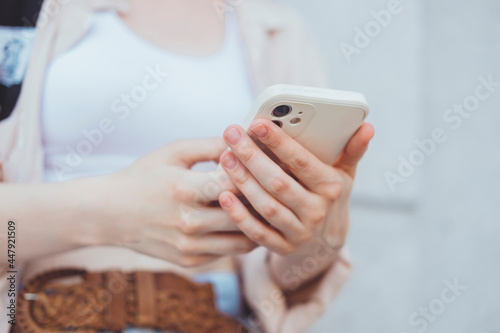 Young blonde woman using smartphone in hand, outdoor hipster portrait, street style, glasses, happy face, backpack, earphones, jacket