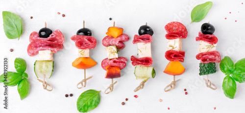 Фотография Mini skewer appetizers with salami, feta cheese, olive, peach and cucumber on the white table