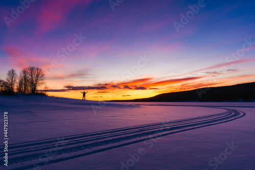 Man standing on frozen and snow covered lake at sunrise