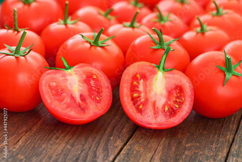 Whole and sliced ripe tomatoes on a wooden table, close up.