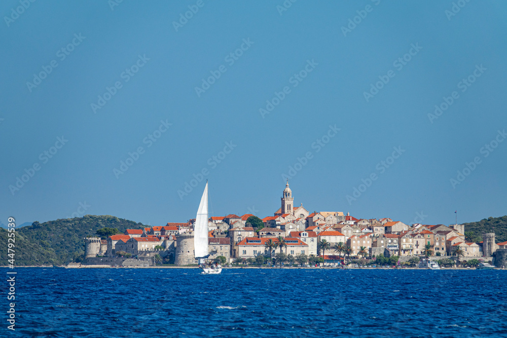 AERIAL: Sailboat sails towards the distant ancient town of Korcula, Croatia.