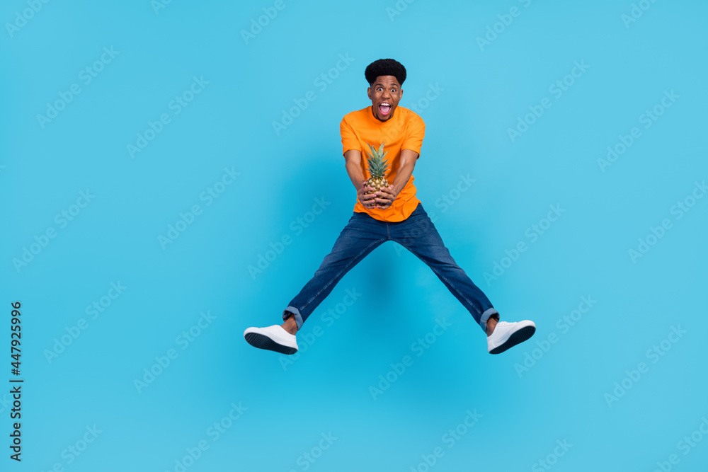 Fototapeta premium Full size photo of hooray brunet millennial guy jump with fruit wear orange t-shirt jeans isolated on blue color background