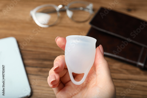 Woman holding white menstrual cup over wooden table, closeup