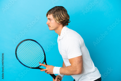 Young blonde man isolated on blue background playing tennis