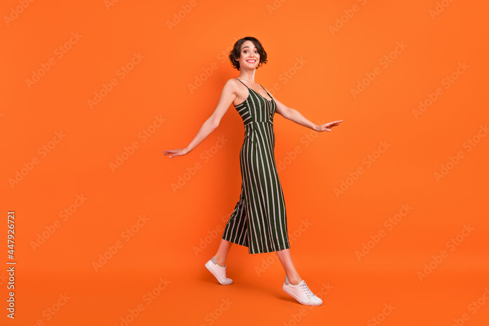 Full length profile photo of joyful brunette millennial lady go wear overall sneakers isolated on orange background Full length profile photo of joyful brunette millennial lady go wear overall sneakers isolated on orange background