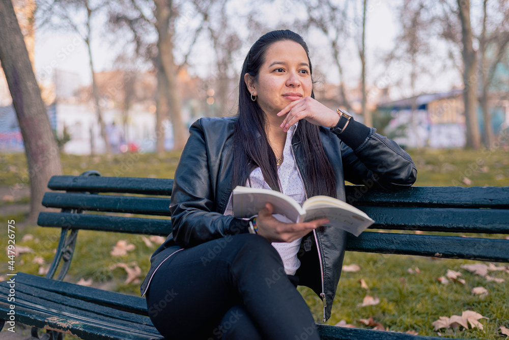 Young woman reading a book at an urban park sitting on a park bench Young woman reading a book at an urban park sitting on a park bench