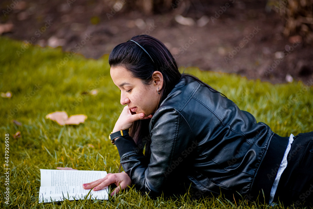 Young woman reading a book lying on the grass at an urban park Young woman reading a book lying on the grass at an urban park