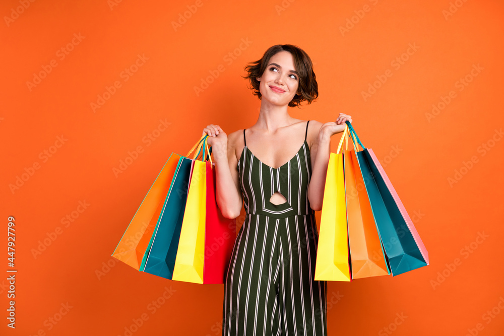 Photo of lovely brunette young lady hold bags look empty space wear overall isolated on orange background