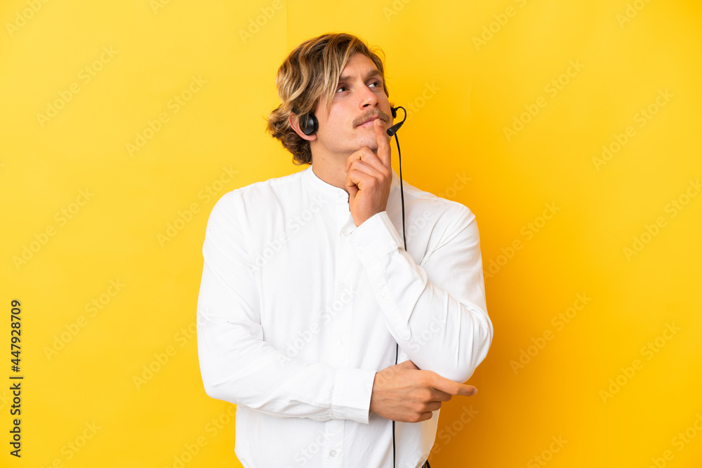 Telemarketer man working with a headset isolated on yellow background having doubts while looking up Telemarketer man working with a headset isolated on yellow background having doubts while looking up