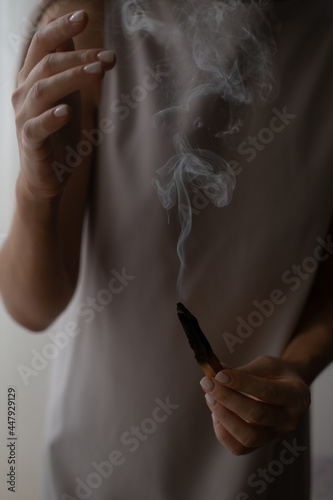 Woman holding in hands palo santo stick, burning smoke, spiritual practice, energy cleanse, healing, meditating concept. Atmospheric moody photo