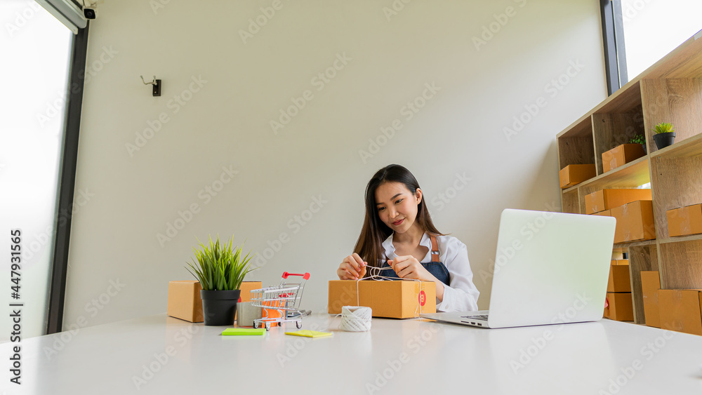 Small business entrepreneur, SME, independent, young Asian woman with box and laptop in small business owner's office in Asia. online marketing packing box delivery SME e-commerce success concept Small business entrepreneur, SME, independent, young Asian woman with box and laptop in small business owner's office in Asia. online marketing packing box delivery SME e-commerce success concept