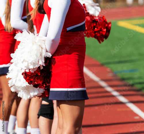 Cheerleader with pompoms behind her back on sidelines watching the ame