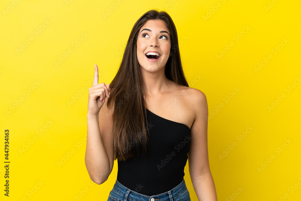 Young Brazilian woman isolated on yellow background intending to realizes the solution while lifting a finger up Young Brazilian woman isolated on yellow background intending to realizes the solution while lifting a finger up