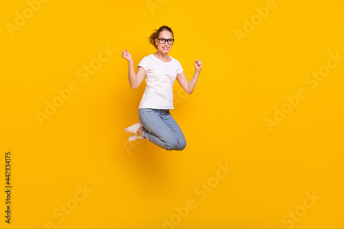 Full body photo of young happy woman jump up raise fists winner celebrate isolated on yellow color background