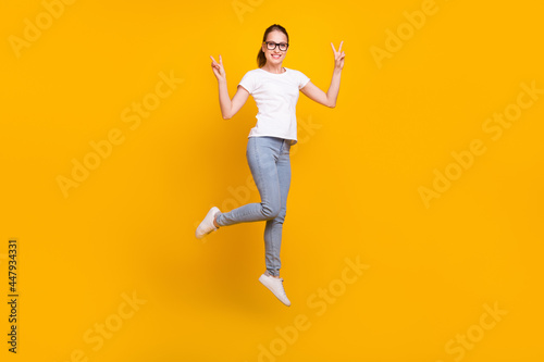 Full length photo of happy enjoy positive woman jump up make v-signs isolated on yellow color background © deagreez
