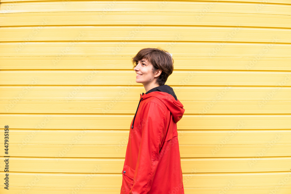Photo of a young girl with a red raincoat smiling with a yellow background behind her.