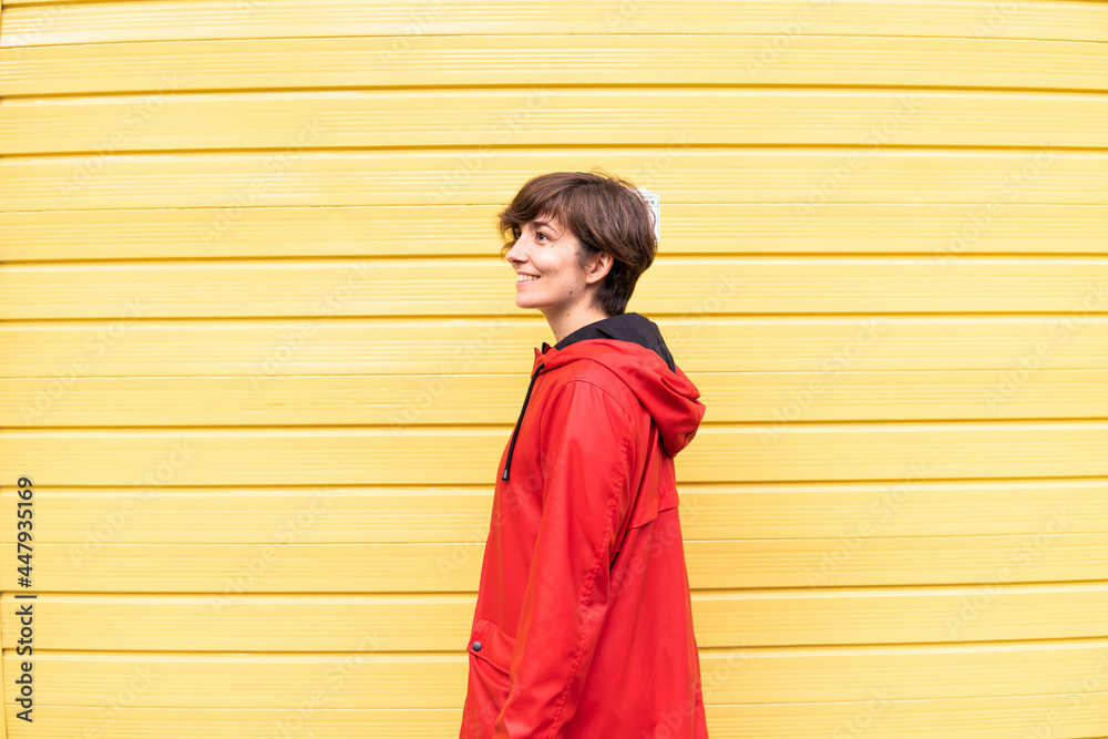 Photo of a young girl with a red raincoat smiling with a yellow background behind her.