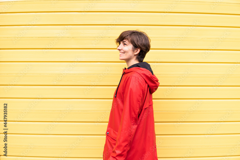 Photo of a young girl with a red raincoat smiling with a yellow background behind her.
