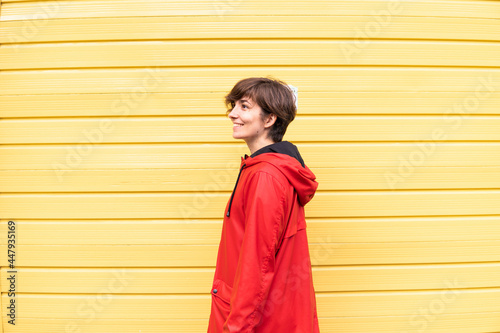 Obraz na płótnie Photo of a young girl with a red raincoat smiling with a yellow background behind her. w salonie