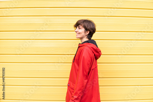 Obraz na płótnie Photo of a young girl with a red raincoat smiling with a yellow background behind her. w salonie