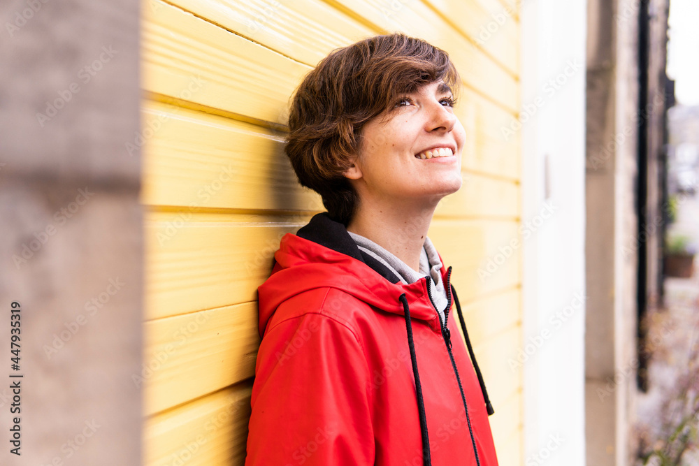 Photo of a young girl with a red raincoat smiling with a yellow background behind her.