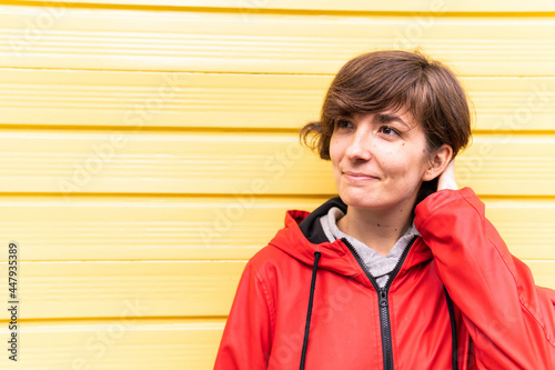Obraz na płótnie Photo of a young girl with a red raincoat smiling with a yellow background behind her. w salonie