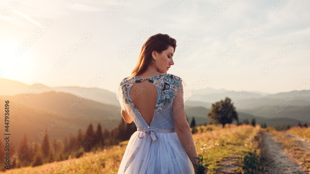 Beautiful bride in blue wedding dress with embroidery and bare back walking in mountains at sunset. Beautiful bride in blue wedding dress with embroidery and bare back walking in mountains at sunset.