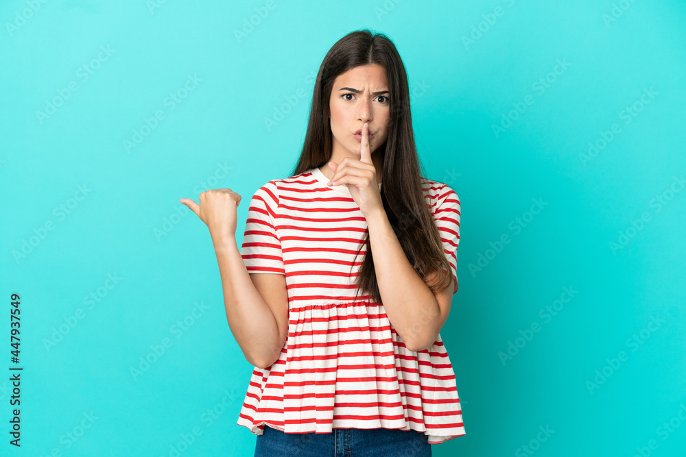 Young Brazilian woman isolated on blue background pointing to the side and doing silence gesture Young Brazilian woman isolated on blue background pointing to the side and doing silence gesture