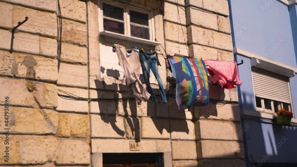 atmospheric video of lisbon. clothes of local residents are dried in the sun on a balcony against the backdrop of beautiful buildings. flowers in pots, good weather, cloudless blue sky.