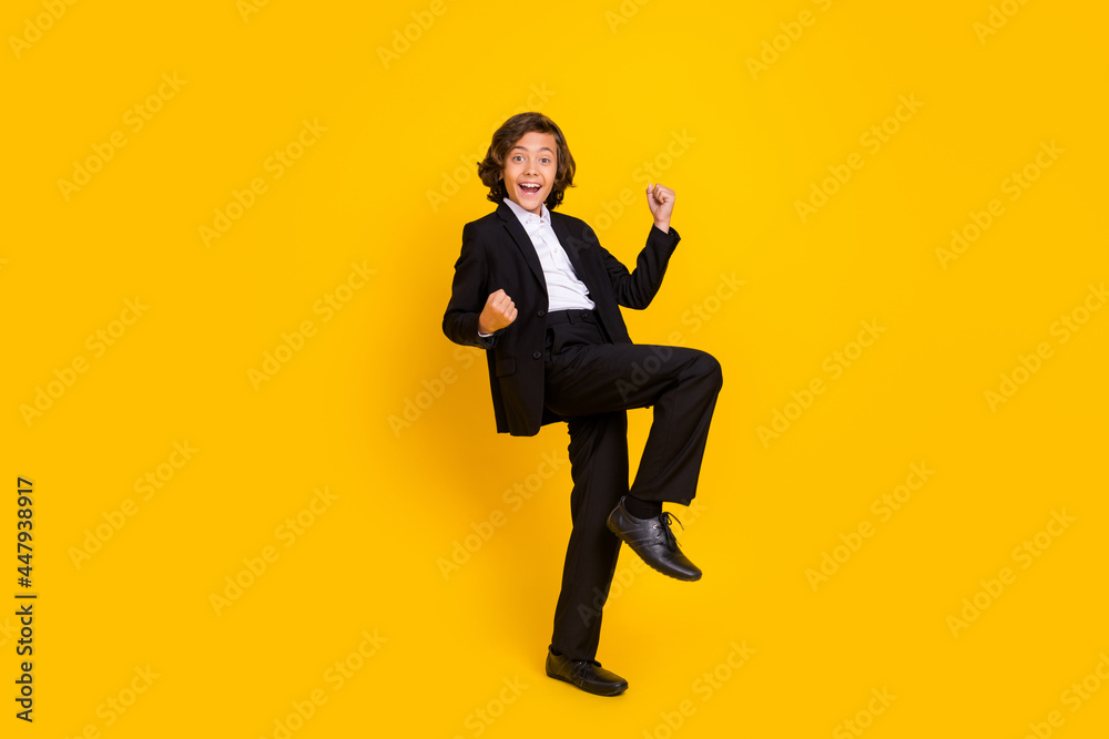 Photo of astonished crazy boy raise fists scream yeah wear black uniform isolated yellow color background Photo of astonished crazy boy raise fists scream yeah wear black uniform isolated yellow color background