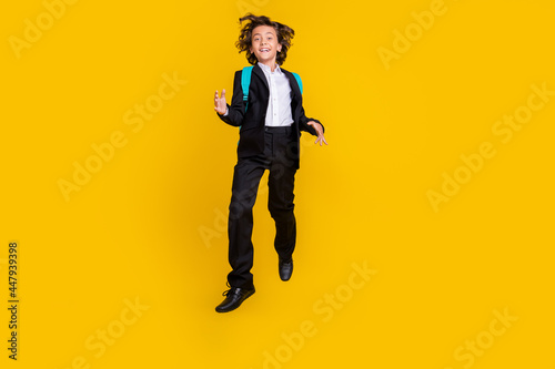 Photo of funky inspired joyful schoolboy jump wear backpack black uniform isolated yellow color background