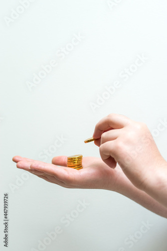 Caucasian hand putting a coin on other hand holding some golden coins on a white background