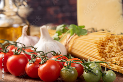 Italian pasta (macaroni), spaghetti tied with sisal string, tomatoes, olive oil, cheese and spices on rustic wood, selective focus.